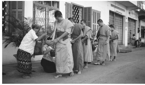 A group of Buddhist monks visit houses at dawn to collect alms in Vientiane.